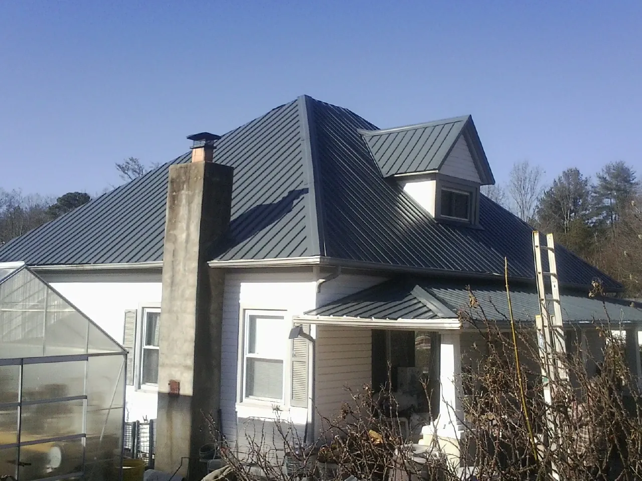 Dark blue standing seam metal roof on a white farmhouse with dormer — Slate & Tile Roof Repair by Roofing Brothers in Watertown