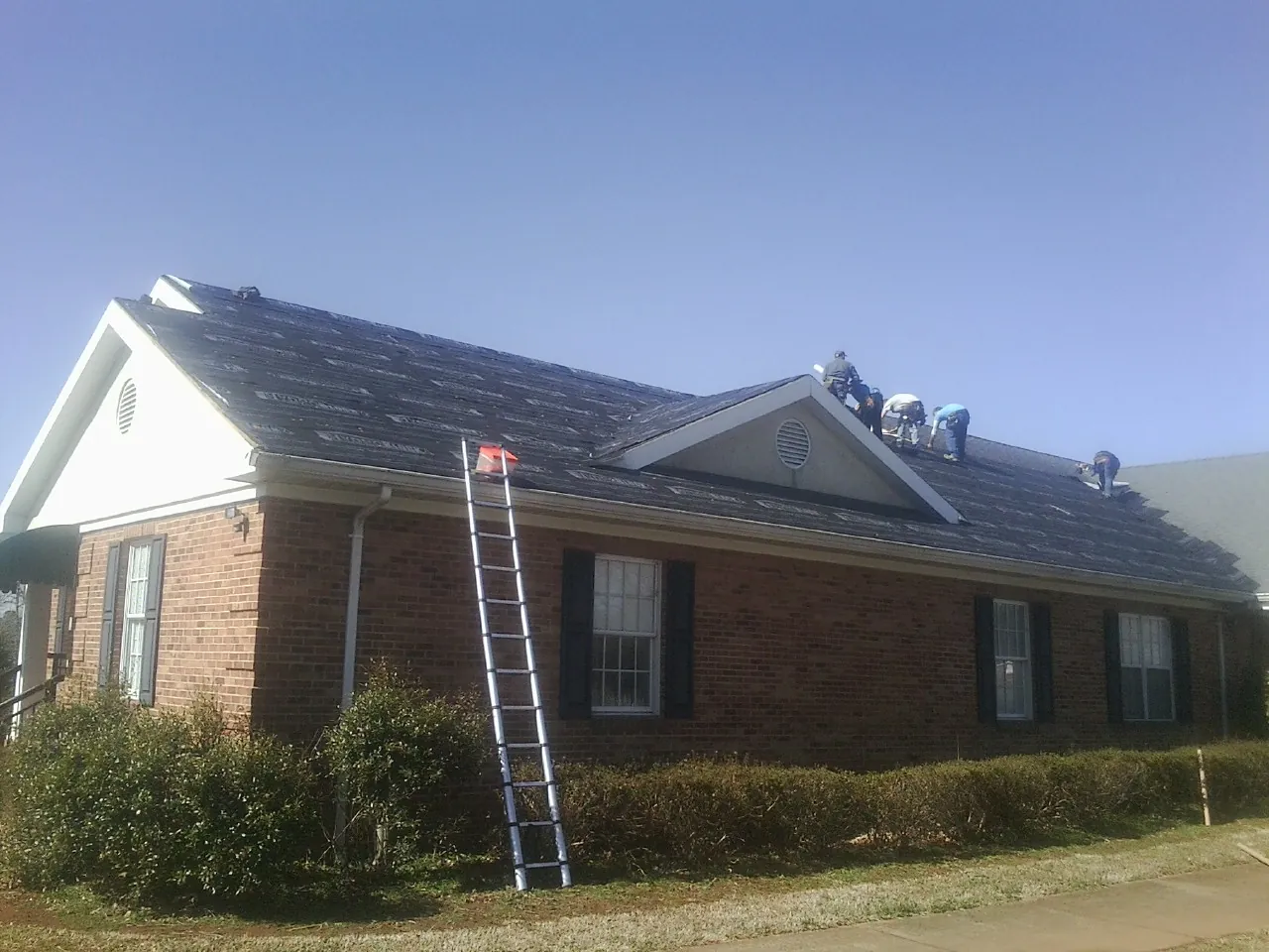 Crew tearing shingles off a brick ranch roof with a ladder set — Metal Roof Repair work by our crew in Watertown